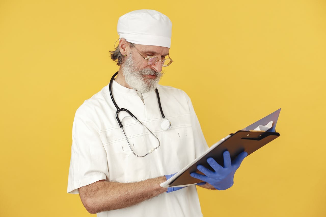 Elderly doctor with stethoscope analyzing clipboard against yellow background.
