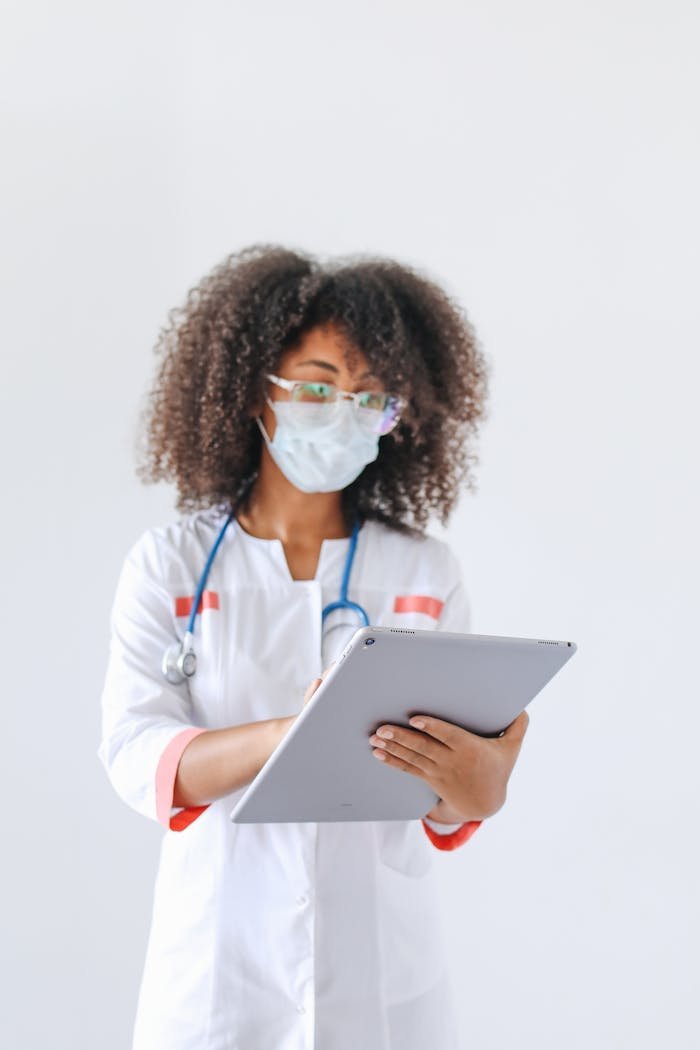 A female doctor wearing a mask uses a tablet in a medical setting, exemplifying modern healthcare.